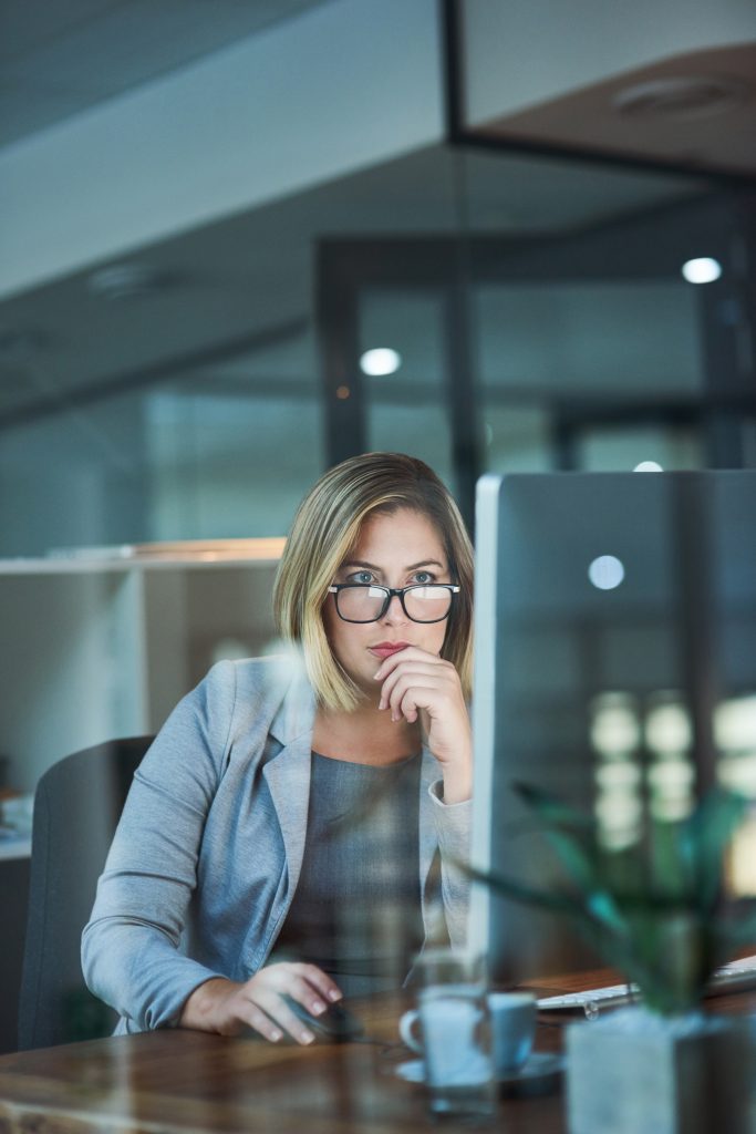 Focused professional woman working on a laptop in a glass office.