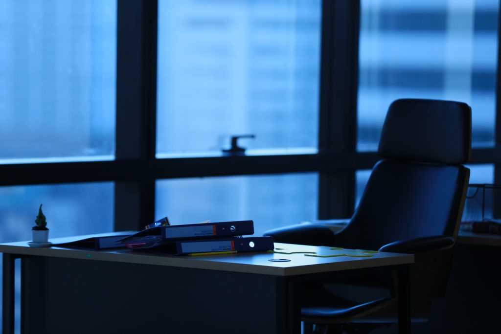 Empty executive office desk facing large windows at dusk.