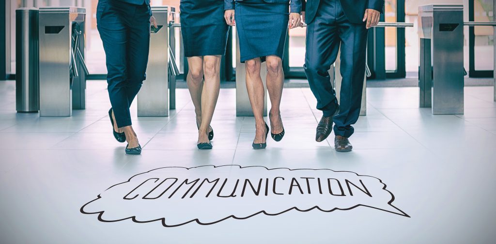 Business professionals walking over the word “communication” on an office floor.