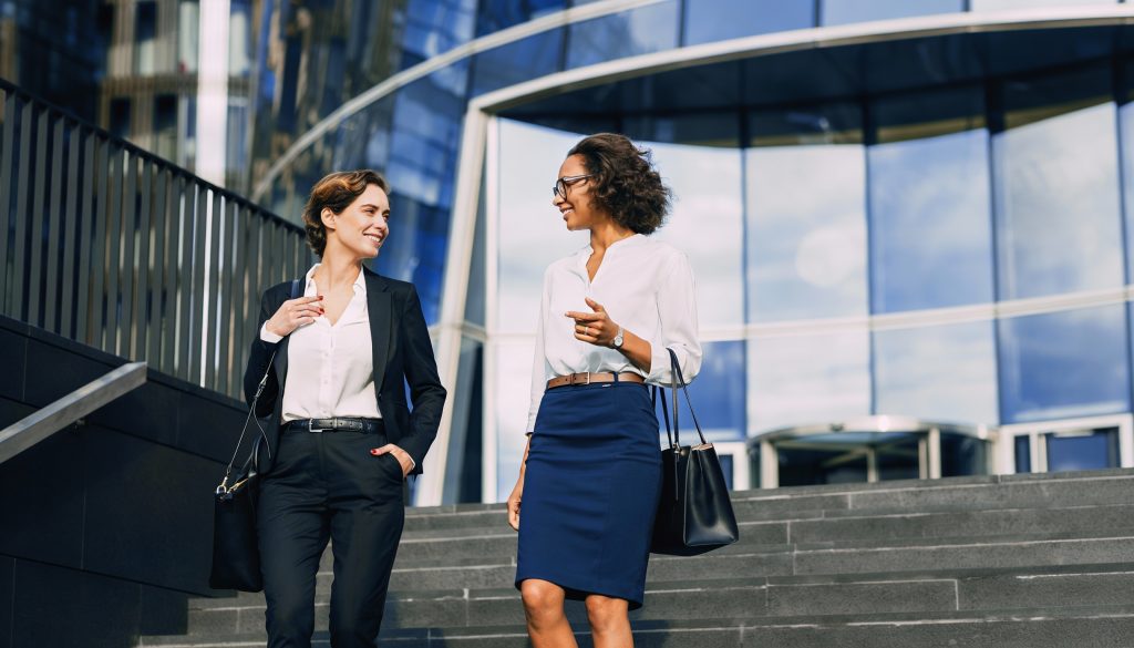 Two businesswomen walking and talking outside a contemporary office building.