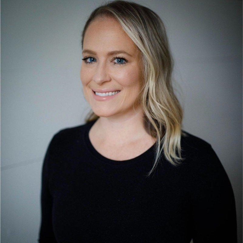 Professional woman smiling in a studio portrait against a neutral background.