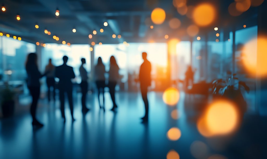 Blurred silhouettes of people walking in a brightly lit office corridor.