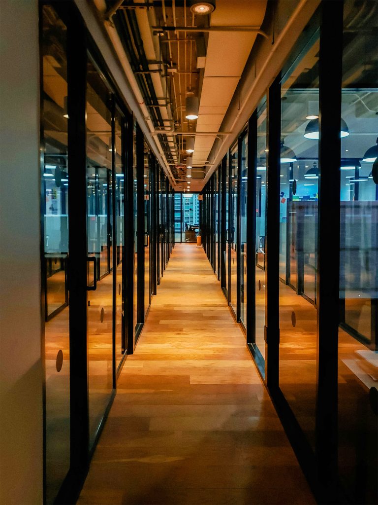 Long glass-walled office corridor with warm lighting and reflections.