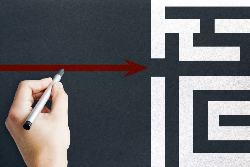 Hand drawing an arrow through a maze toward a clear exit path.