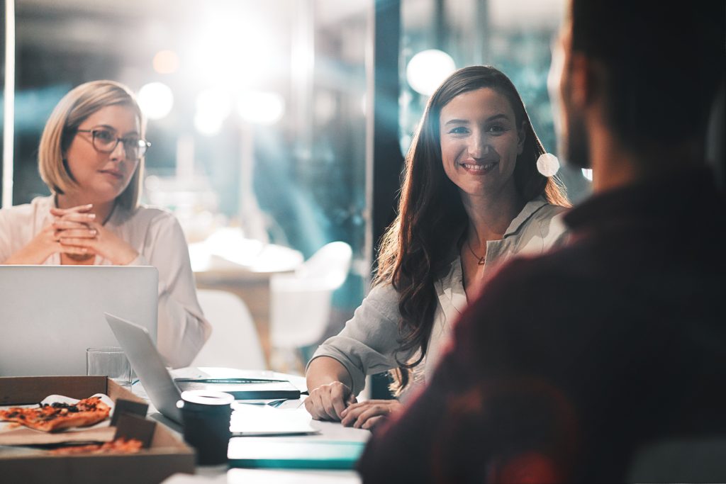 Team members talking and smiling around a table in an office meeting.