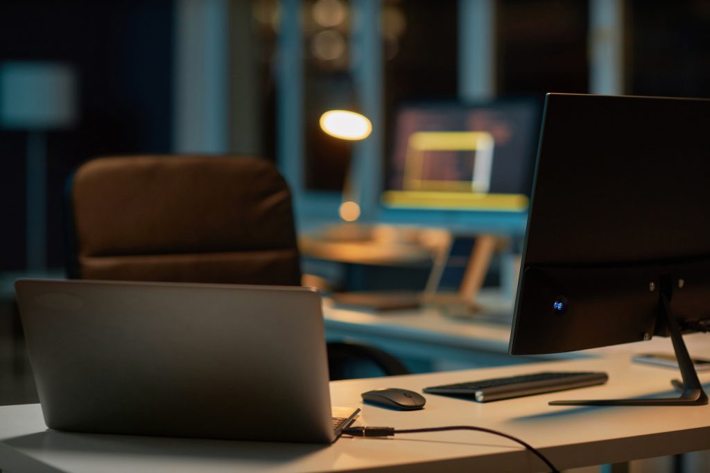 Desk with open laptop and office equipment in a dimly lit workspace.