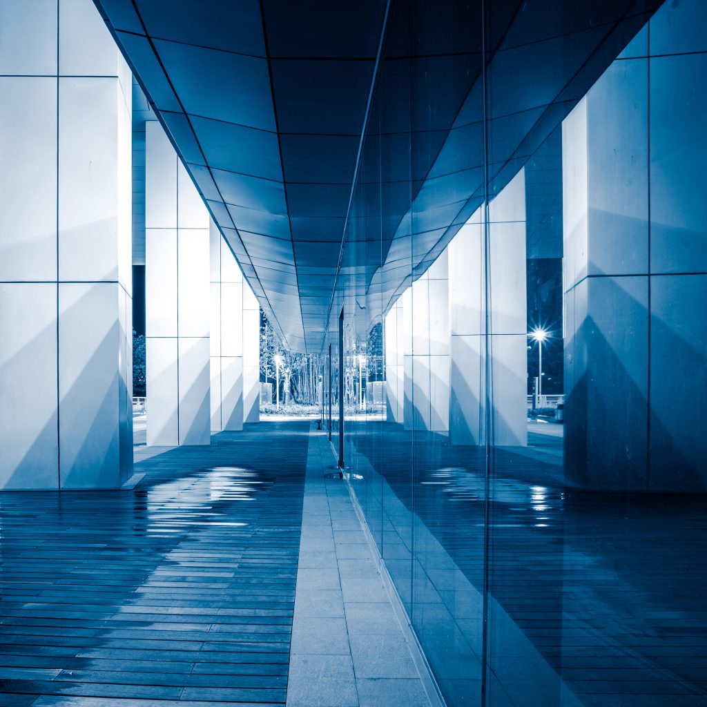 Long modern corridor with glass walls and reflections in an office building.