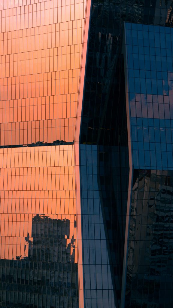 Modern glass skyscraper reflecting warm sunset light in a city skyline.