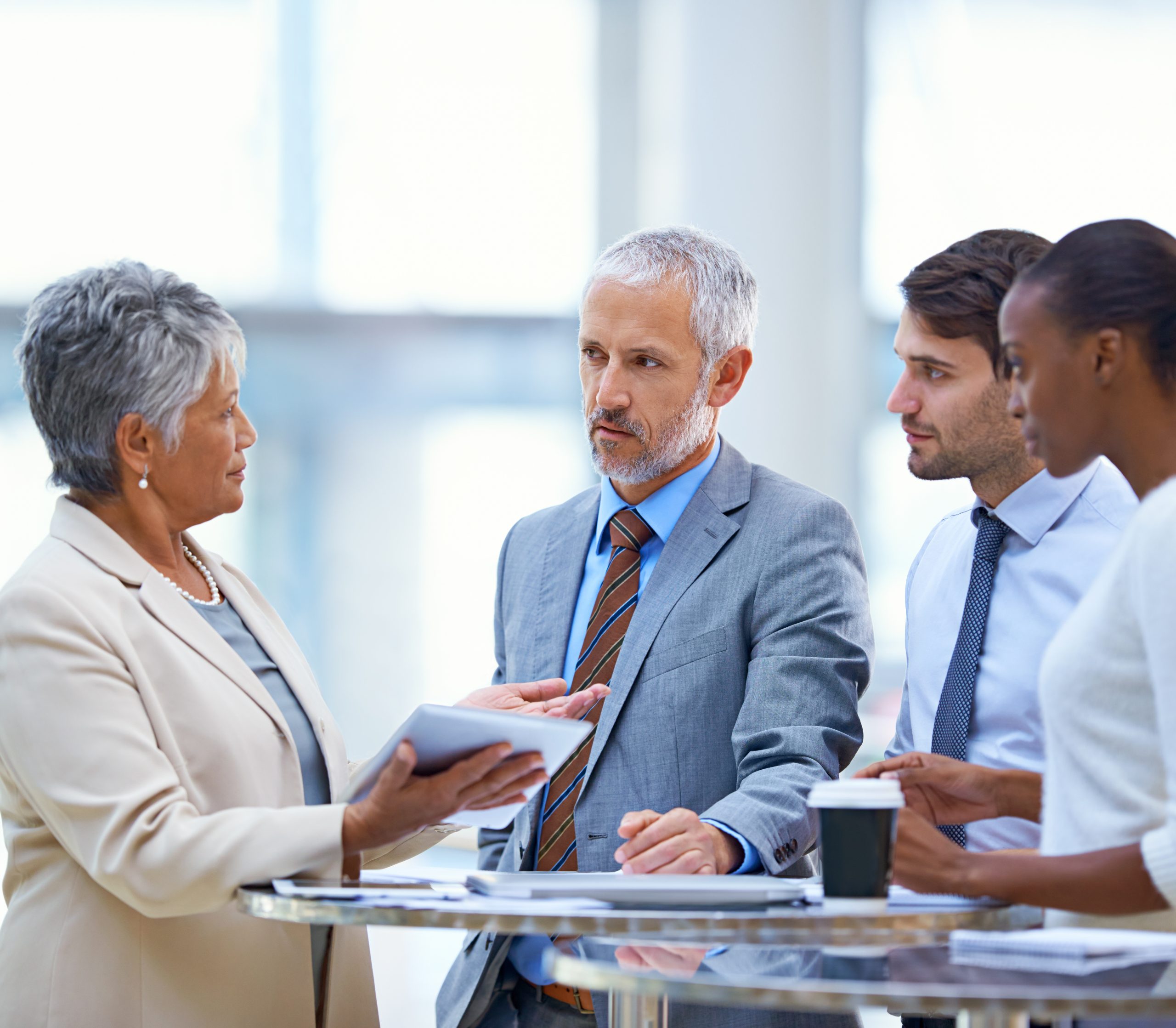 A group of people in business attire stand around a table and interact with one another.