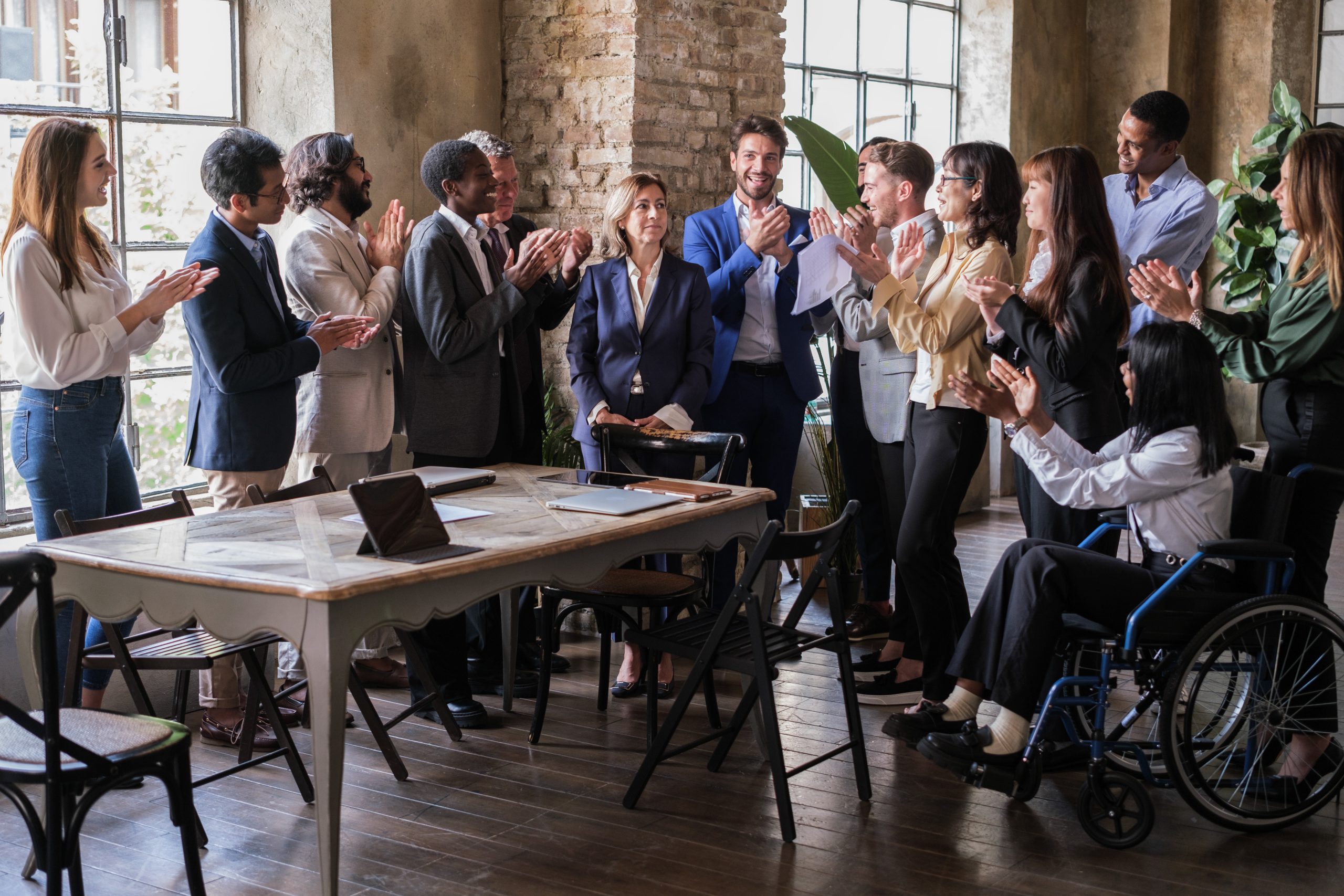 A group of business professionals clap and cheer for their coworker, who stands with her arms in front of her.